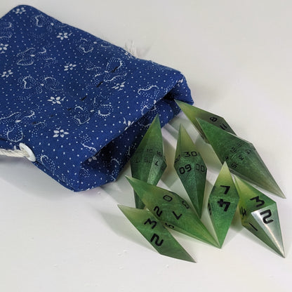 Swirling shades of green with black numbering diamond handmade dice spilling out of a blue and white drawstring bag on a white background. The set features 2 d20s and matching resin dice, showcasing the unique shape of these artisan dice.