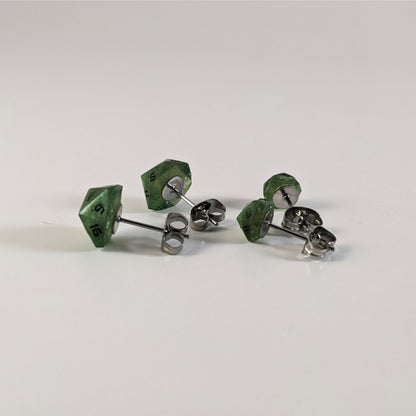 Two pairs of handmade d20 earrings that are shimmering green with black numbers turned to show the metal alloy hardware and butterfly backs.