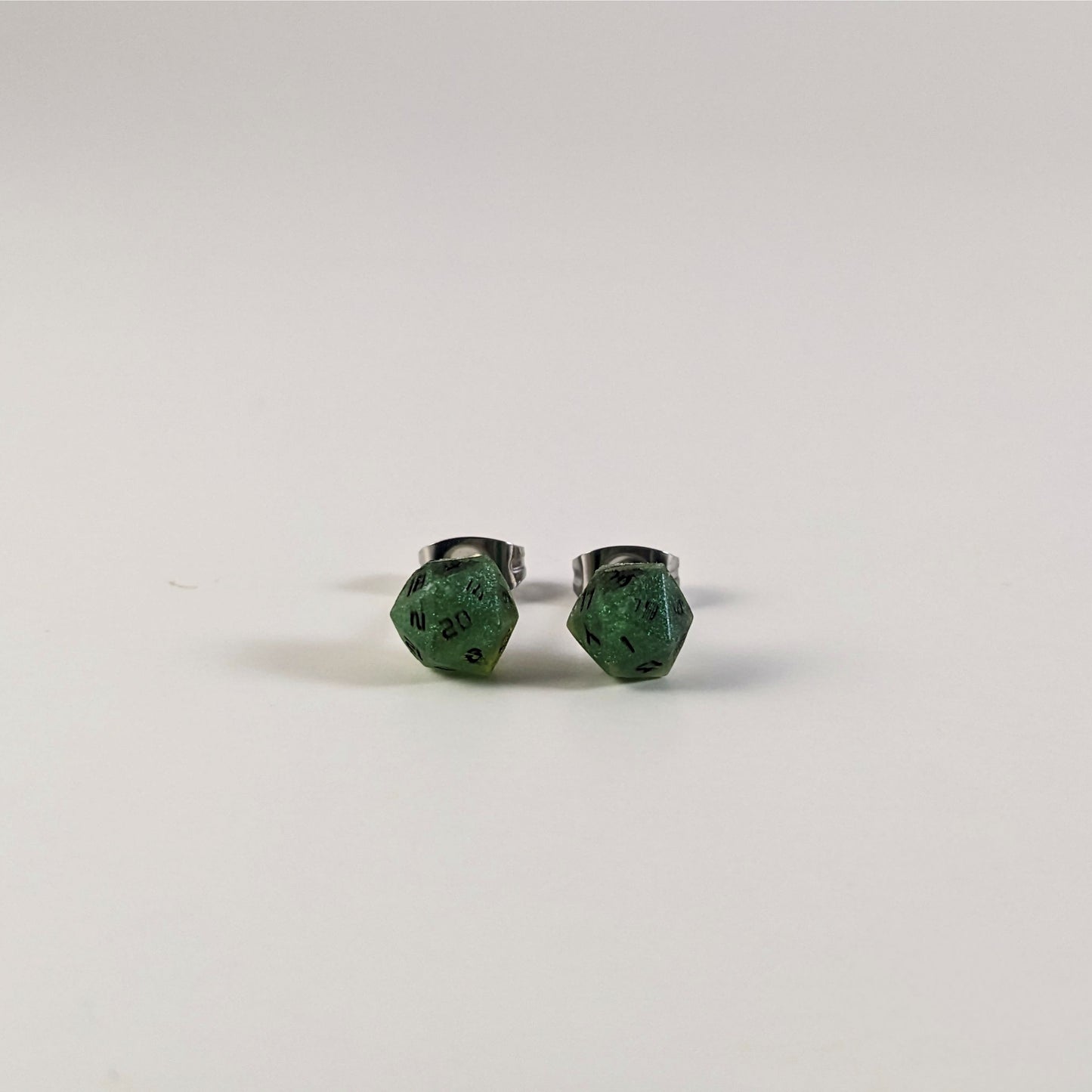 A single pair of the smaller size handmade d20 earrings that are shimmering green with black numbers on a white background. The earring on the left centers the 20 face and the earring on the right centers the 1 face.