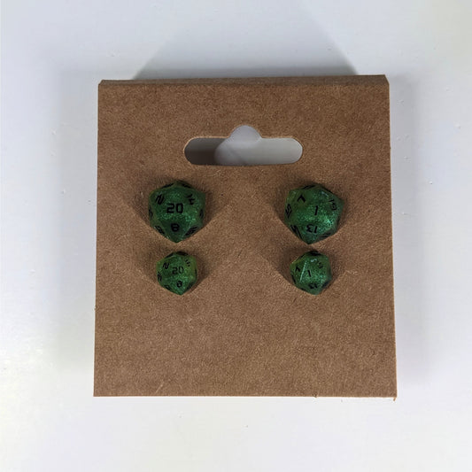 Two pairs of handmade d20 earrings that are shimmering green with black numbers on a kraft brown earring card. The earrings on the left of each pair centers the 20 face and the earrings on the right of each pair centers the 1 face.