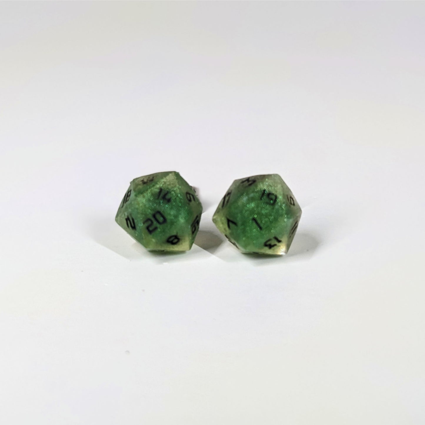 A single pair of the larger size handmade d20 earrings that are shimmering green with black numbers on a white background. The earring on the left centers the 20 face and the earring on the right centers the 1 face.