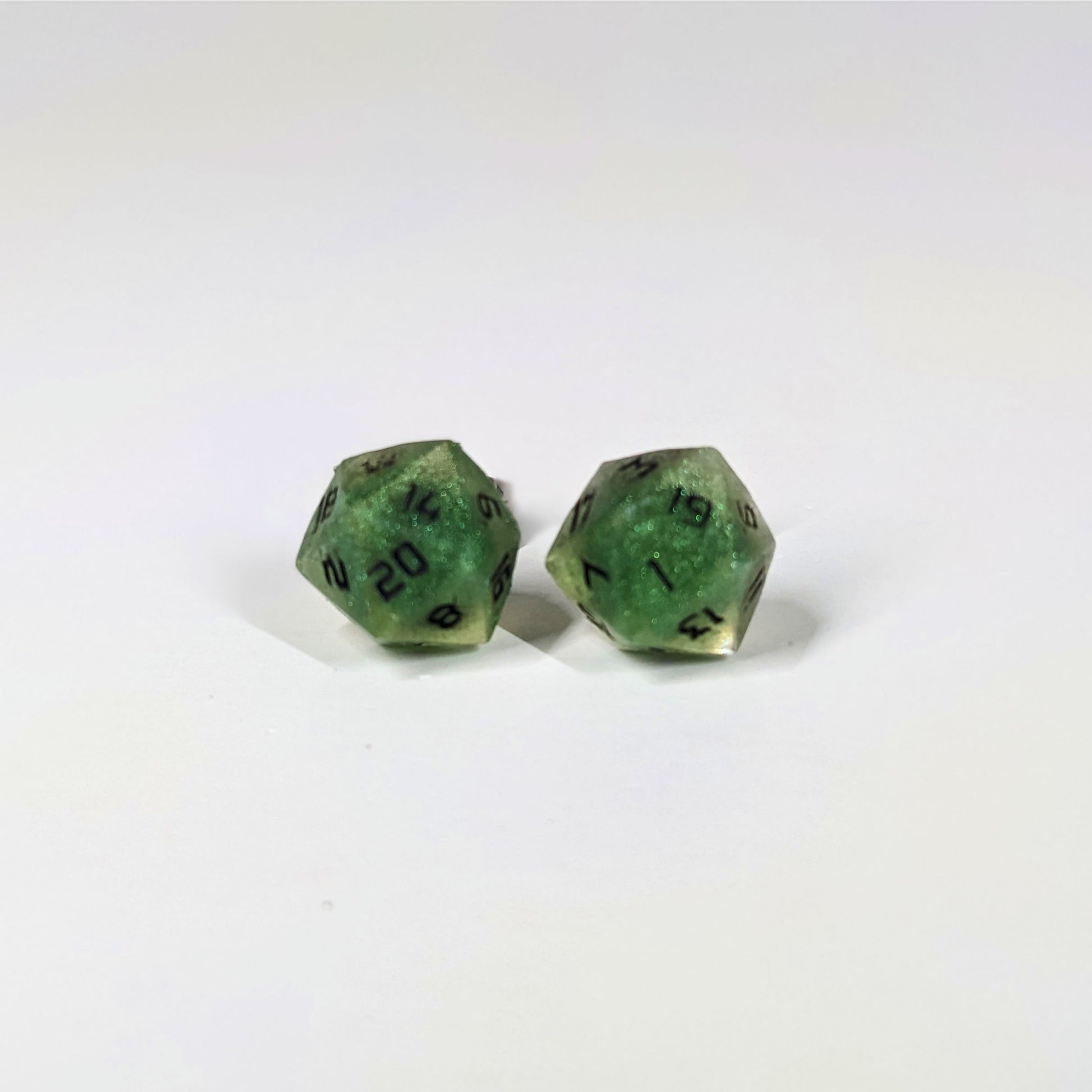 A single pair of the larger size handmade d20 earrings that are shimmering green with black numbers on a white background. The earring on the left centers the 20 face and the earring on the right centers the 1 face.