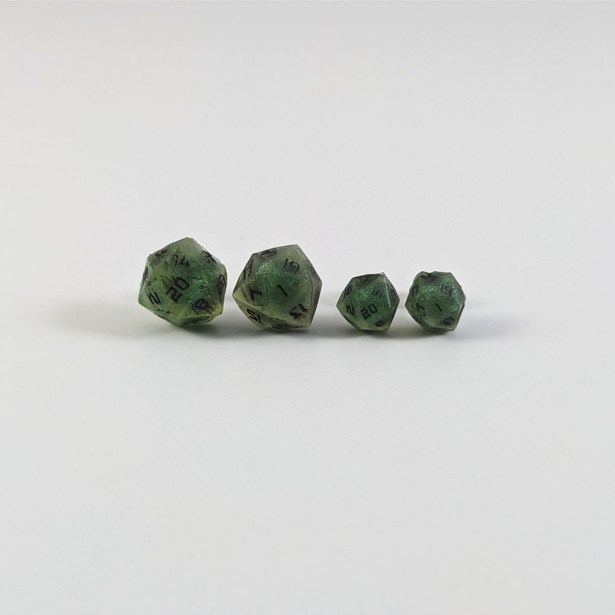 Two pairs of handmade d20 earrings with titanium hardware that are swirls of green with black numbers on a white background sit in a line with the larger pair on the left and the smaller pair on the right. The earrings on the left of each pair centers the 20 face and the earrings on the right of each pair centers the 1 face.