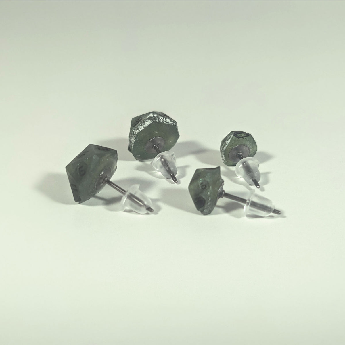 Two pairs of handmade d20 earrings that are swirls of green with black numbers turned to show the titanium hardware and bell shaped rubber backs.