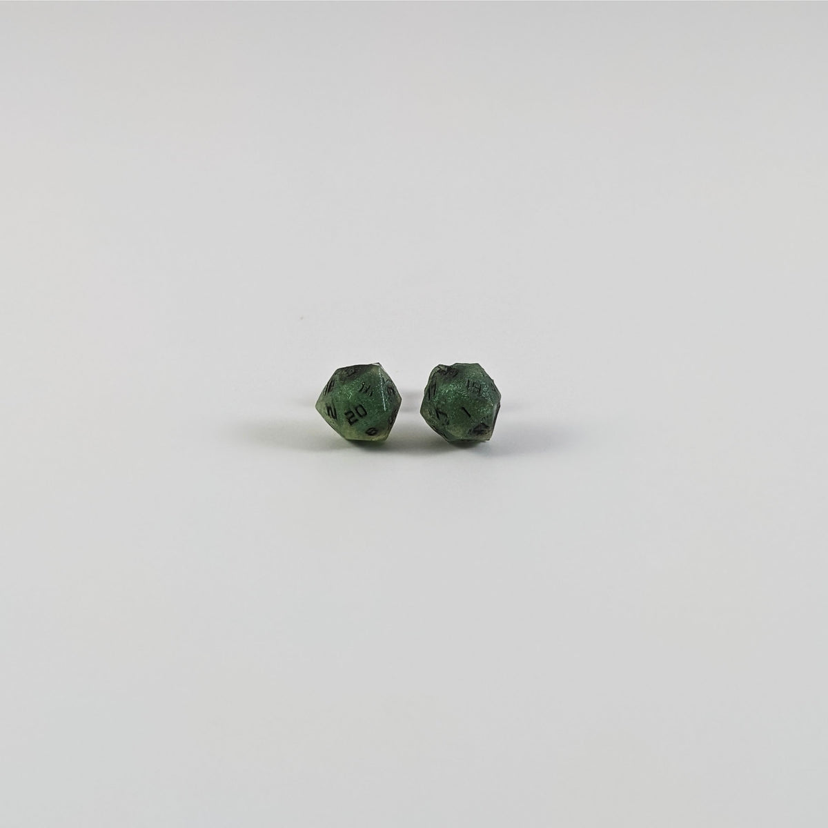 A single pair of the smaller size handmade d20 earrings with titanium hardware that are swirls of green with black numbers on a white background. The earring on the left centers the 20 face and the earring on the right centers the 1 face.