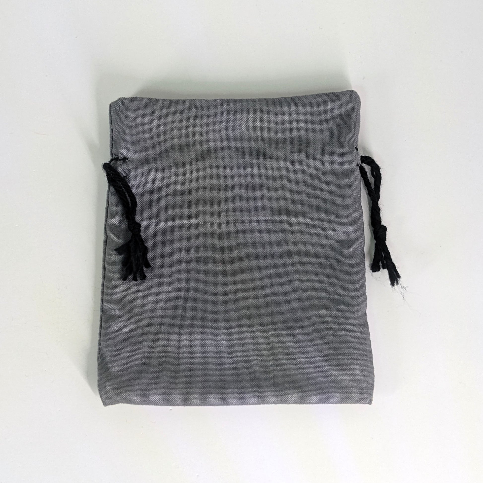 A small, handmade dice bag that is gray lays flat on a white background.