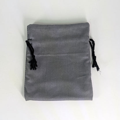 A small, handmade dice bag that is gray lays flat on a white background.