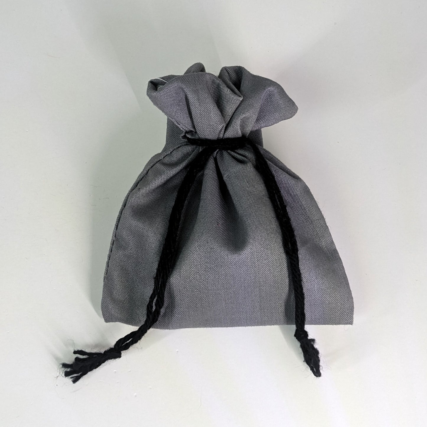 A small, handmade dice bag that is gray is tied closed on a white background.