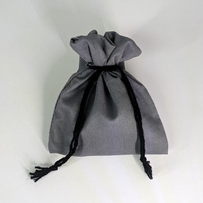 A small, handmade dice bag that is gray is tied closed on a white background.