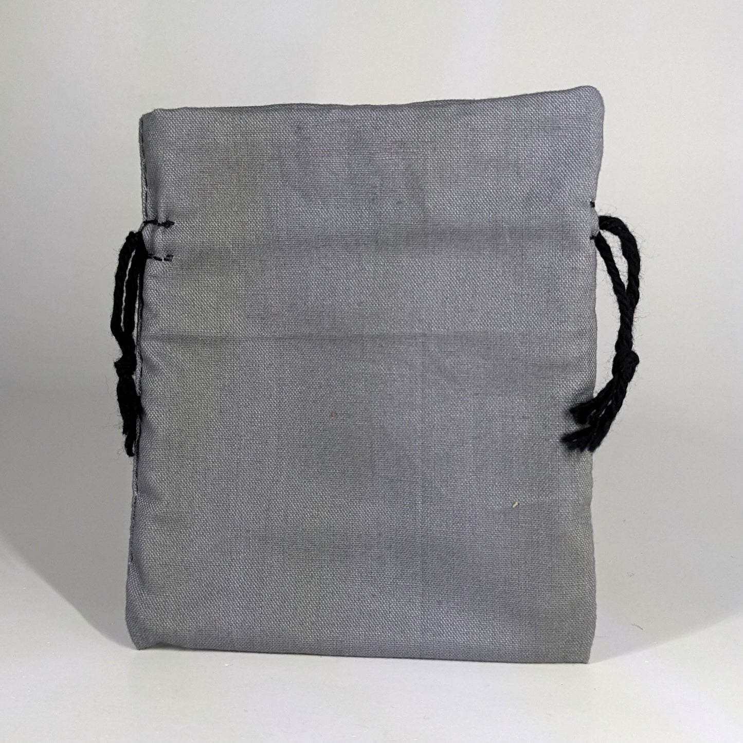 A small, handmade dice bag that is gray stands upright on a white background.
