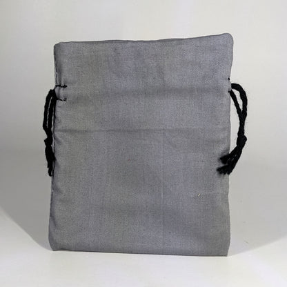 A small, handmade dice bag that is gray stands upright on a white background.