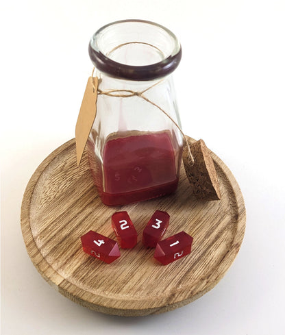 A glass bottle sits open on a wooden circle. The cork stopper rests propped up on the side of the glass bottle. Inside the bottle is red resin to look like liquid healing potion. Four small red crystal d4s rest in front of the bottle in an arc with the 4, 2, 3, and 1 faces up from left to right.