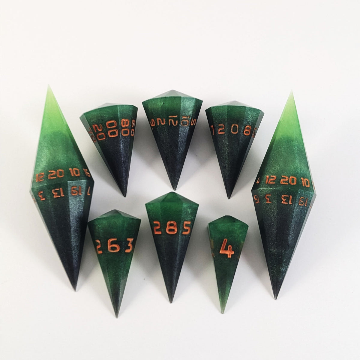 A dagger style DnD dice set that is  green and black with orange numbers that glow in the dark is arranged with a d20 each on the right and left, with the d%, d12, and d10 along the top and the d6, d8, and d4 along the bottom, all in line with the d20s.