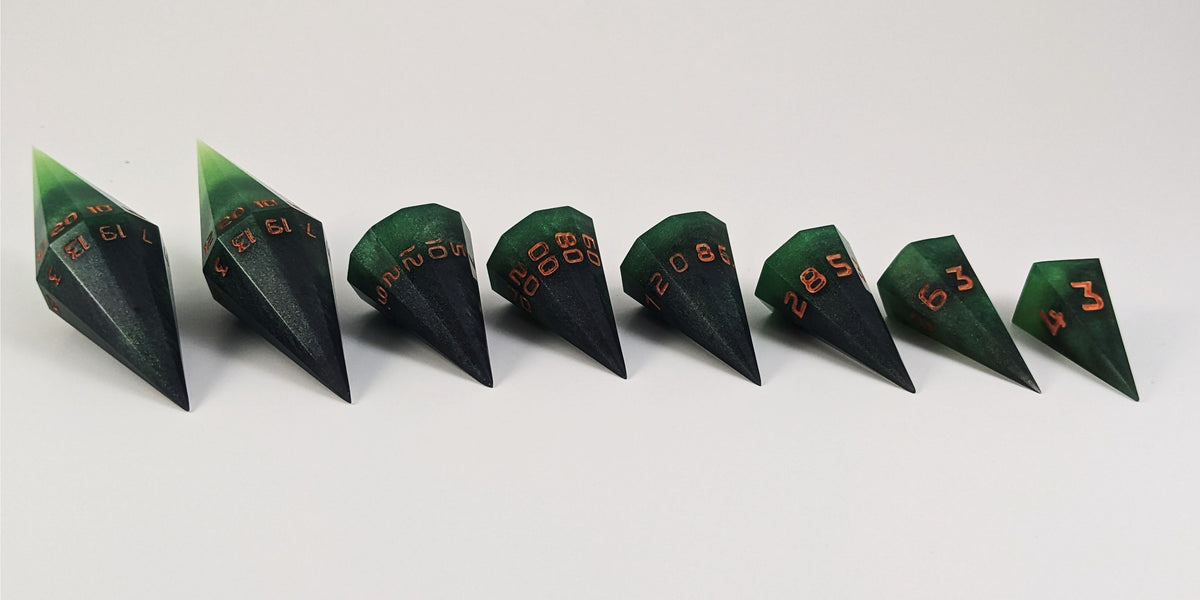 A straight on photo of a complete set of dagger DnD dice that are black and green with orange numbers that glow in the dark arranged in a straight line with points angled toward the right. They are lined up with the 2 d20s on the left going down to the d4 on the right side. The highest value number of each die is facing forward.