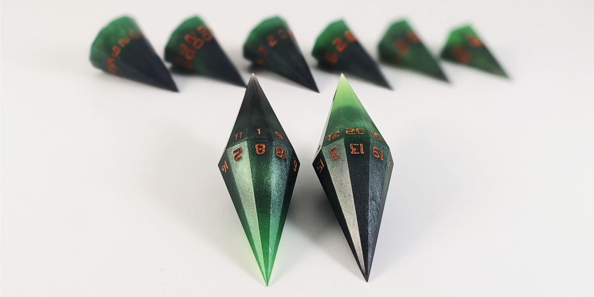 A straight on photo of a dagger set of DnD dice that are green and black with orange numbers that glow in the dark focusing on 2 d20s in the center. The d20 on the left has the 1 face up and the d20 on the right has the 20 face up. The other 6 dice are lined up in the background but are out of focus, while the d20s are in sharp focus.