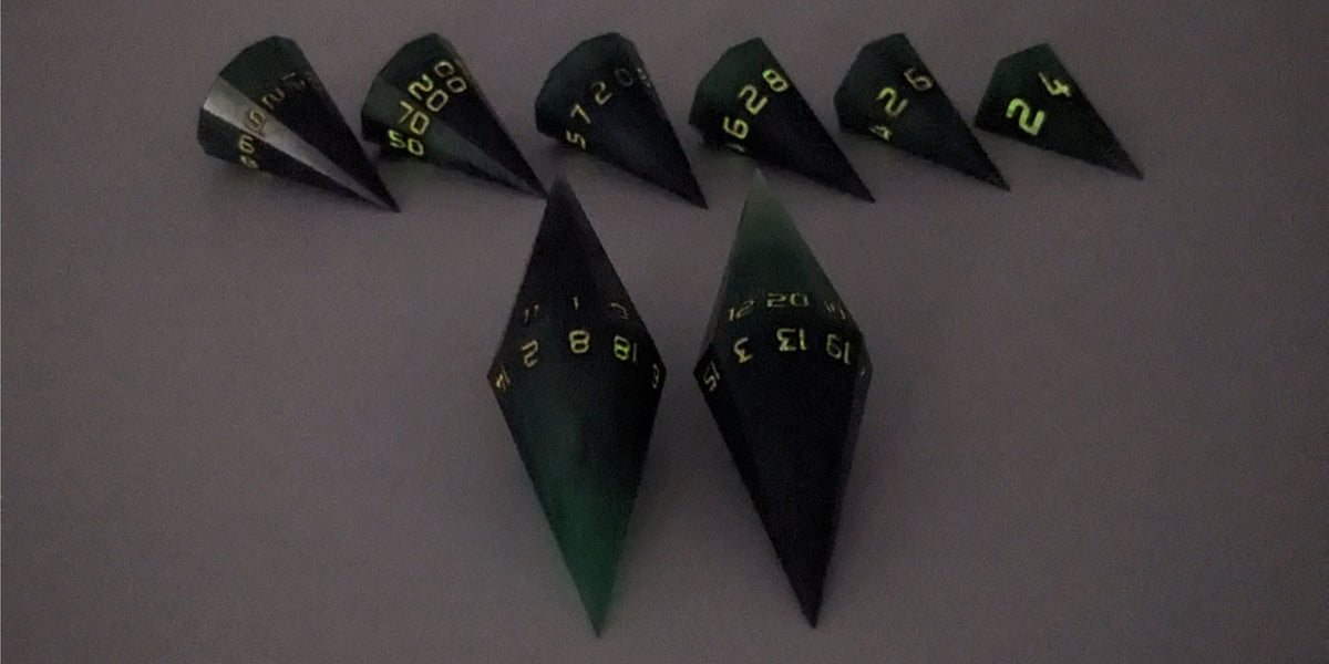 A straight on photo of a dagger set of DnD dice that are green and black with orange numbers that glow in the dark focusing on 2 d20s in the center. The d20 on the left has the 1 face up and the d20 on the right has the 20 face up. The other 6 dice are lined up in the background but are out of focus, while the d20s are in sharp focus. The photo is taken in the dark to show the orange numbers glowing green.