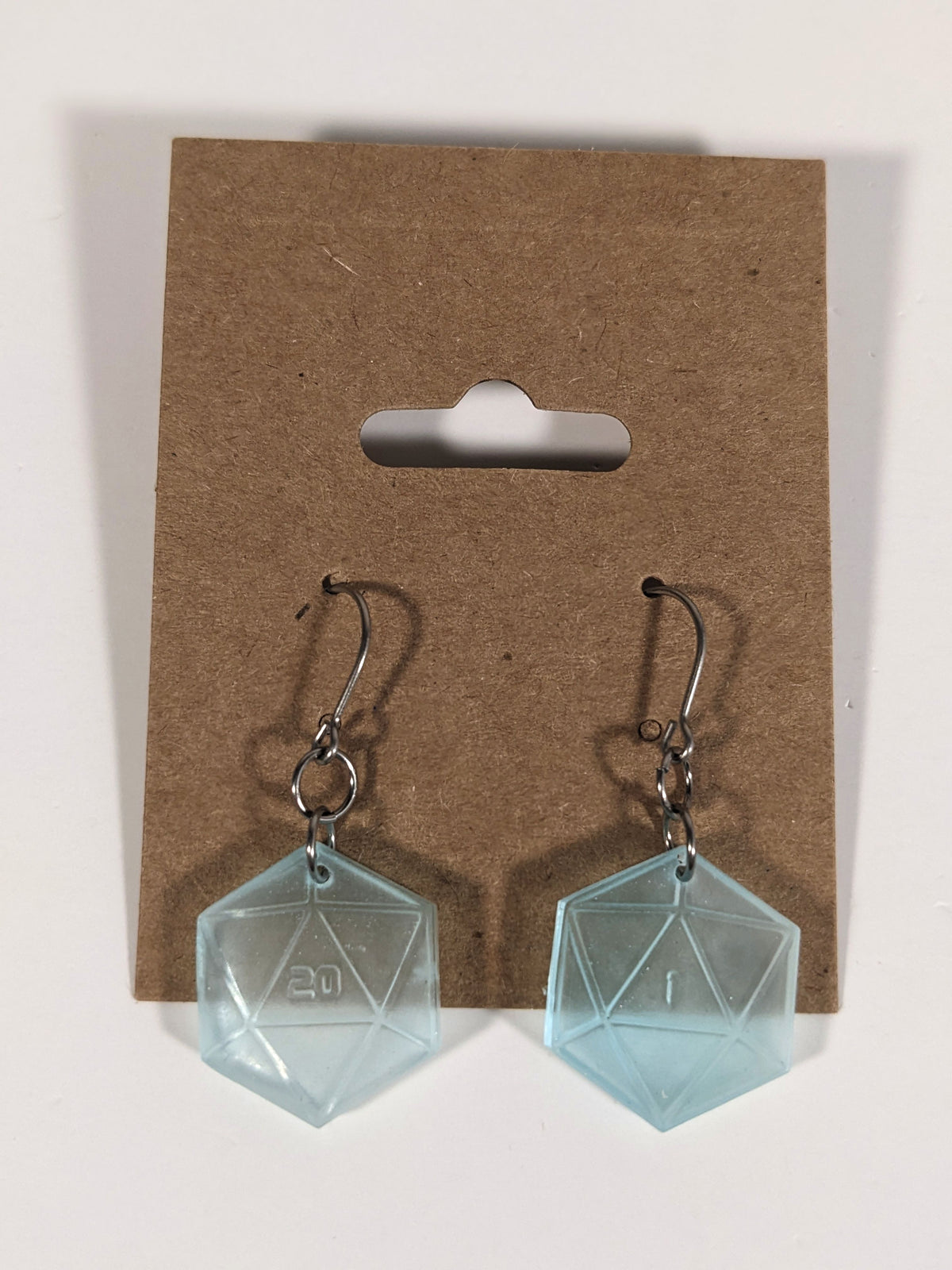 A pair of frosty blue and white dangly, flat d20 earrings with silver color titanium and niobium hardware on a kraft earring card on a white background. The earring on the left has a 20 on it and the earring on the right has a 1 on it, both in a sci-fi style font.