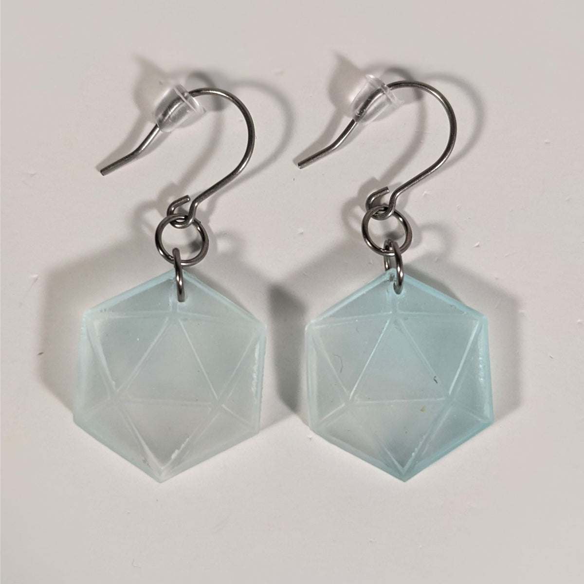 A pair of frosty blue and white dangly, flat d20 earrings with silver color titanium and niobium hardware and bell shaped rubber backs on a white background.