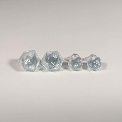Two pairs of handmade d20 earrings with titanium hardware that are frosty blue and white with white numbers on a white background sit in a line with the larger pair on the left and the smaller pair on the right. The earrings on the left of each pair centers the 20 face and the earrings on the right of each pair centers the 1 face.