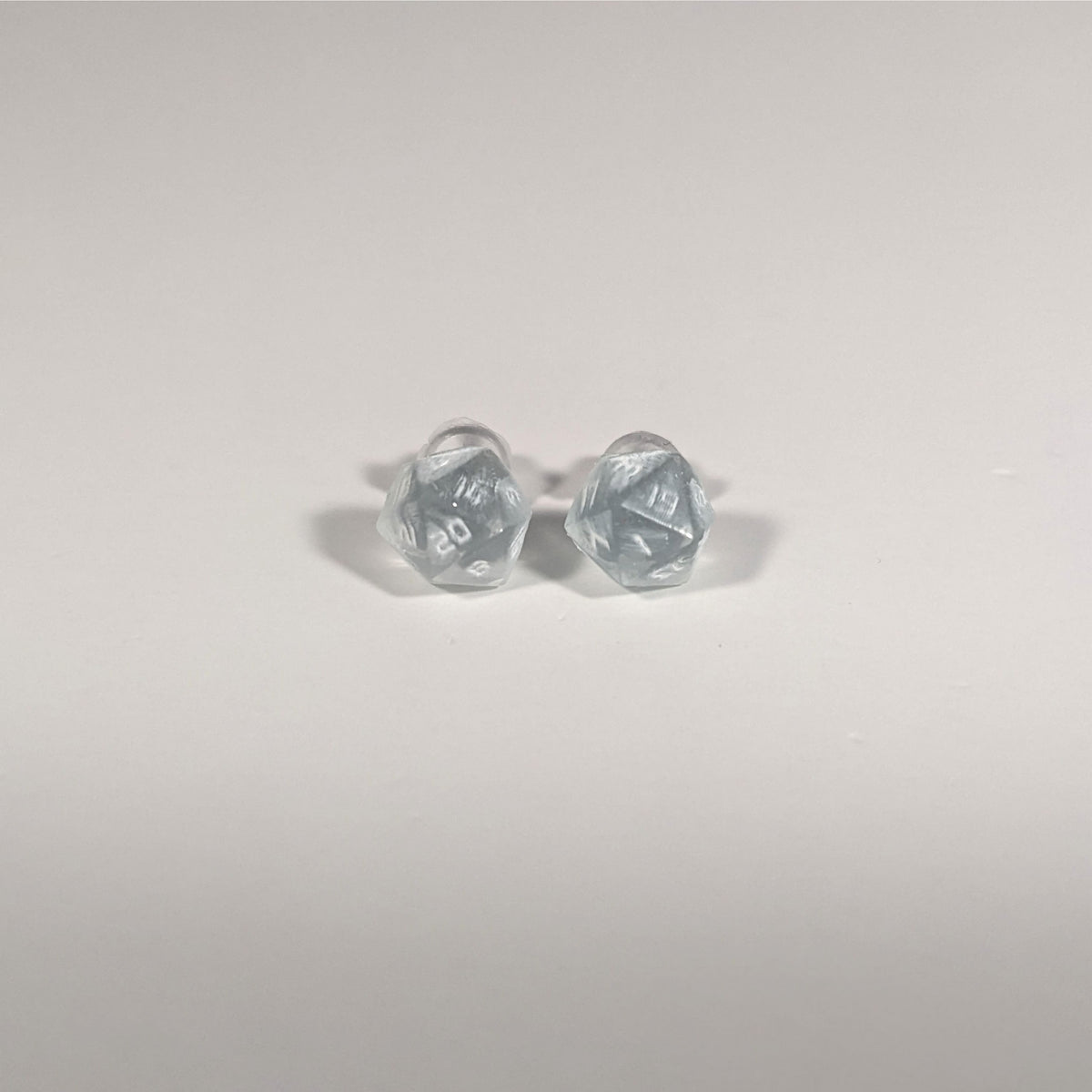 A single pair of the smaller size handmade d20 earrings with titanium hardware that are frosty blue and white with white numbers on a white background. The earring on the left centers the 20 face and the earring on the right centers the 1 face.