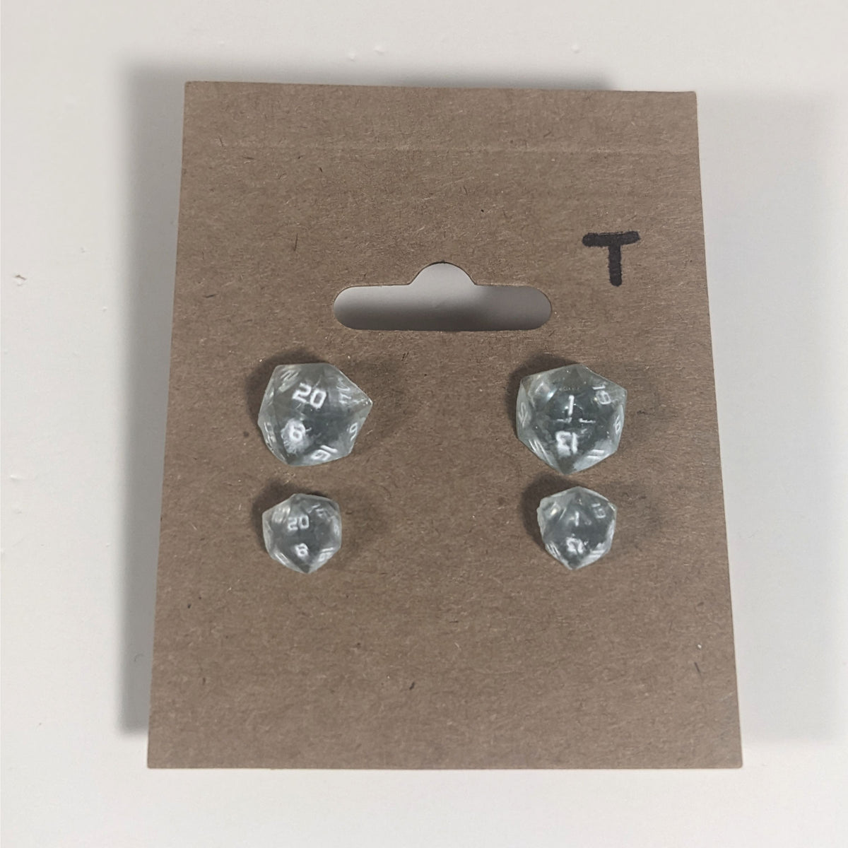Two pairs of handmade d20 earrings with titanium hardware that are frosty blue and white with white numbers on a kraft brown earring card with a T in the top right corner. The earrings on the left of each pair centers the 20 face and the earrings on the right of each pair centers the 1 face.