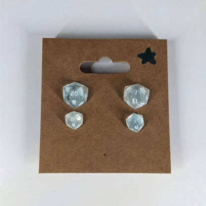 Two pairs of handmade d20 earrings with sterling silver hardware that are transparent white with hints if glittery blue with opaque numbers on a kraft brown earring card with a star in the top right corner. The earrings on the left of each pair centers the 20 face and the earrings on the right of each pair centers the 1 face.