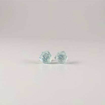 A single pair of the larger size handmade d20 earrings with sterling silver hardware that are transparent white with hints of glittery blue with opaque white numbers on a white background. The earring on the left centers the 20 face and the earring on the right centers the 1 face.