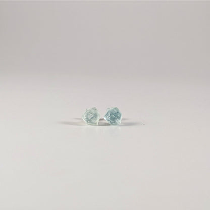 A single pair of the smaller size handmade d20 earrings with sterling silver hardware that are transparent white and hints of glittery blue with opaque white numbers on a white background. The earring on the left centers the 20 face and the earring on the right centers the 1 face.