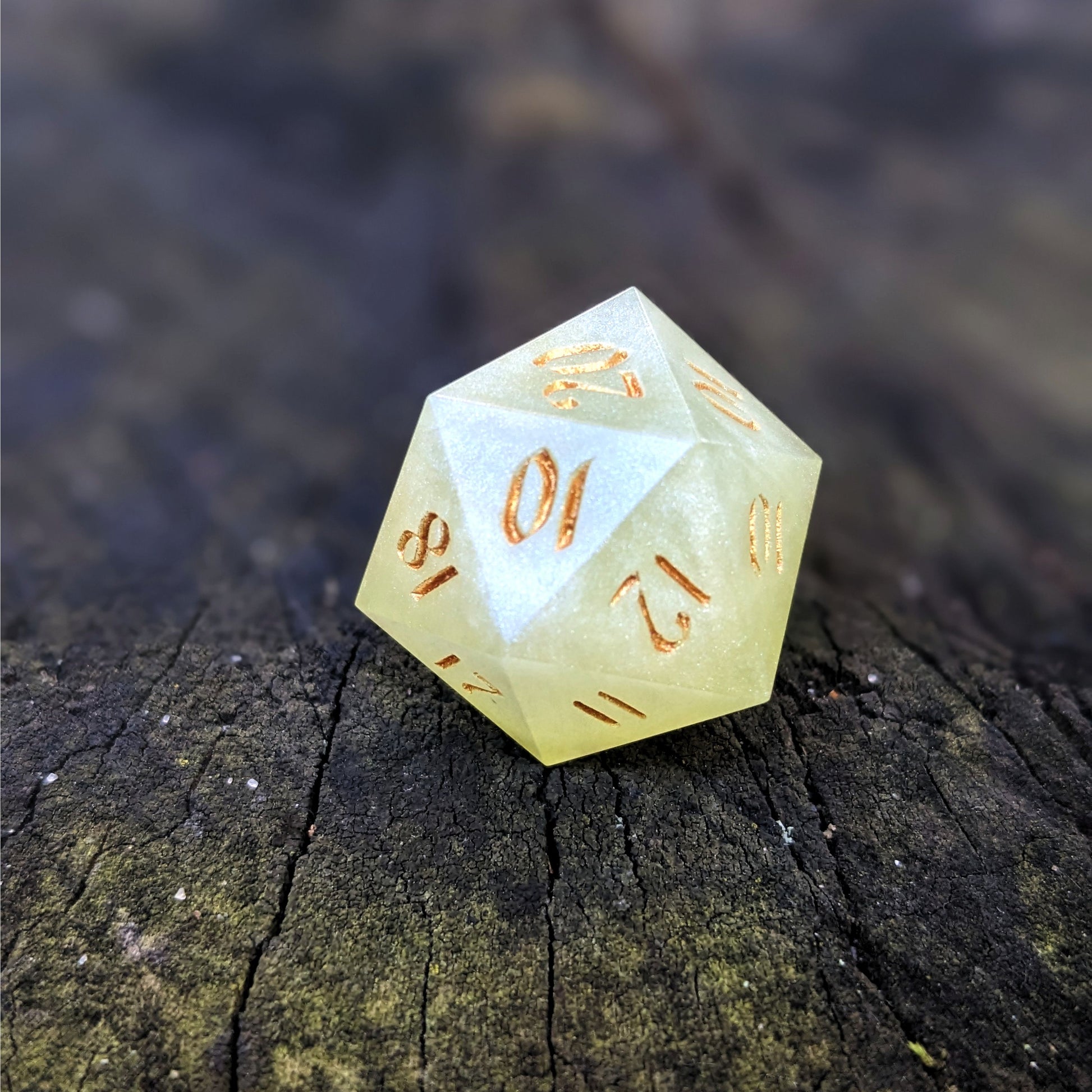 A close up photo of a light green reliable talent d20 with gold numbers sitting on a wood stump. Faces that would be 9 or below are replaced with a 10.