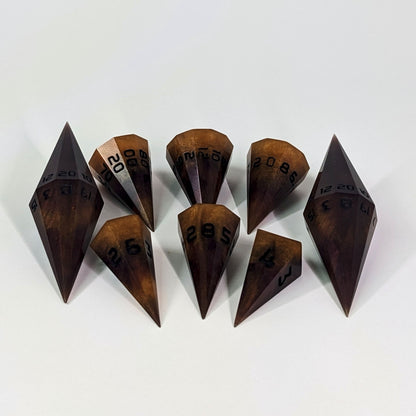 A dagger style DnD dice set that is bright orange tempered with deep red like cooling lava with obsidian black numbers is arranged with a d20 each on the right and left, with the d%, d12, and d10 along the top and the d6, d8, and d4 along the bottom, all in line with the d20s.