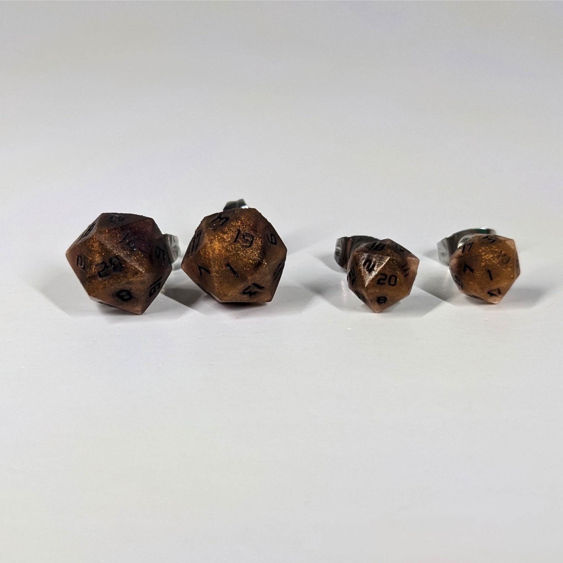 Two pairs of handmade d20 earrings that are orange and deep red with black numbers on a white background sit in a line with the larger pair on the left and the smaller pair on the right. The earrings on the left of each pair centers the 20 face and the earrings on the right of each pair centers the 1 face.