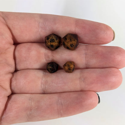 Two pairs of handmade d20 earrings that are orange and deep red with black numbers held between the fingers of a flat hand. The larger pair is between the pointer and middle finger, the smaller between the middle and ring finger. The earrings on the left of each pair centers the 20 face and the earrings on the right of each pair centers the 1 face.