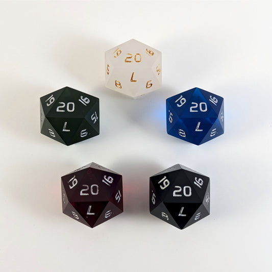 Five spindown d20s with a left spin arranged in a circle with the 20 face on top. White with gold numbers is at the top and blue, black, red, and dark green all with silver numbers follow going clockwise.