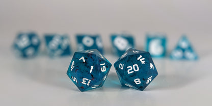 A straight on photo of a standard set of DnD dice that are blue with red flakies and white numbers focusing on 2 d20s in the center. The d20 on the left has the 1 face centered and the d20 on the right has the 20 face centered. The other 6 dice are lined up in the background but are out of focus, while the d20s are in sharp focus.