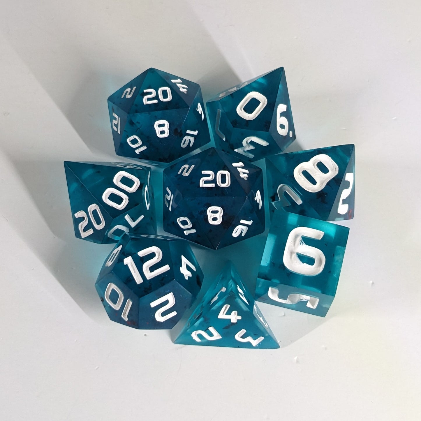 A complete set of 8 handmade artisan dice that are blue with red flakies and white numbers. The DnD dice set is arranged in a circle and features 2 D20s, one of which is in the center surrounded by the other 7 dice. 