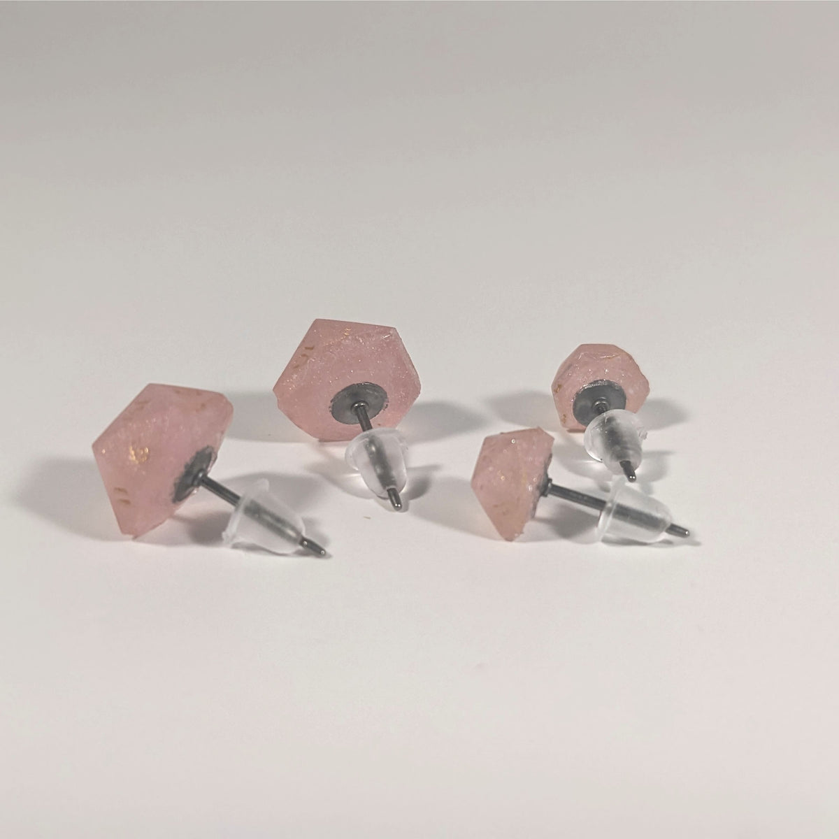 Two pairs of handmade d20 earrings that are pastel pink with gold numbers turned to show the titanium hardware and bell shaped rubber backs.