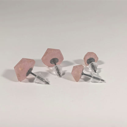 Two pairs of handmade d20 earrings that are pastel pink with gold numbers turned to show the titanium hardware and bell shaped rubber backs.