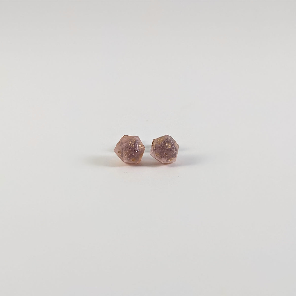 A single pair of the smaller size handmade d20 earrings with titanium hardware that are pastel pink with gold numbers on a white background. The earring on the left centers the 20 face and the earring on the right centers the 1 face.