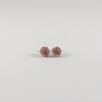 A single pair of the smaller size handmade d20 earrings with titanium hardware that are pastel pink with gold numbers on a white background. The earring on the left centers the 20 face and the earring on the right centers the 1 face.