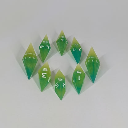 A complete set of resin dice featuring 2 d20s for advantage rolls. These yellow and teal swirls with white numbers and slender handmade diamond dice are clustered in a tight circle on a white background, highlighting the quality of the artisan dice craftsmanship and the unique pointed shape.