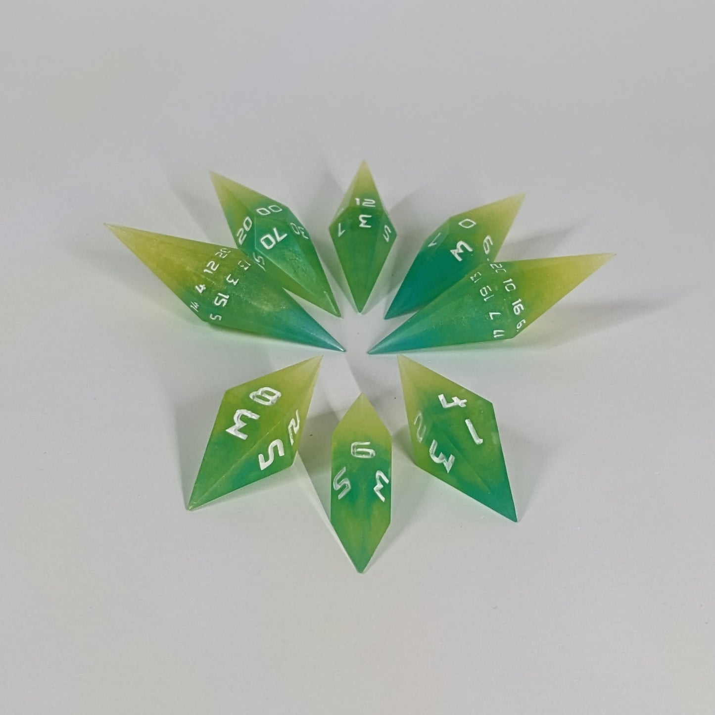  A complete set of resin dice featuring 2 d20s for advantage rolls. These yellow and teal swirls with white numbers and slender handmade diamond dice are clustered in a tight circle on a white background, highlighting the quality of the artisan dice craftsmanship and the unique pointed shape.