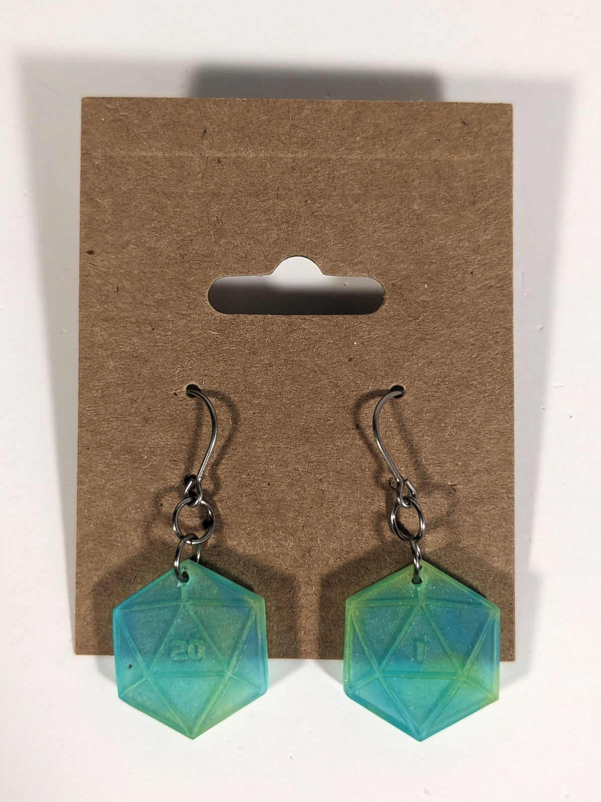A pair of teal and yellow dangly, flat d20 earrings with silver color titanium and niobium hardware on a kraft earring card on a white background. The earring on the left has a 20 on it and the earring on the right has a 1 on it, both in a sci-fi style font.