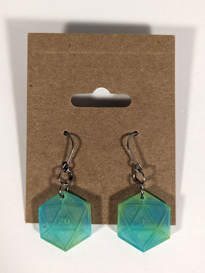 A pair of teal and yellow dangly, flat d20 earrings with silver color titanium and niobium hardware on a kraft earring card on a white background. The earring on the left has a 20 on it and the earring on the right has a 1 on it, both in a sci-fi style font.