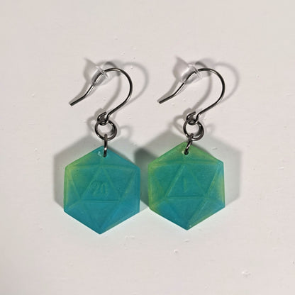 A pair of teal and yellow dangly, flat d20 earrings with silver color titanium and niobium hardware and bell shaped rubber backs on a white background. The earring on the left has a 20 on it and the earring on the right has a 1 on it, both in a fantasy style font.