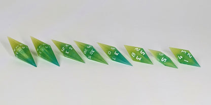 A mid angle photo of a complete set of handmade diamond DnD dice that are yellow and teal swirls with white numbers arranged in a straight line with bottom points angled slightly forwards and towards the right. They are lined up with the 2 d20s on the left going down to the d4 on the right side. The highest value number of each die is facing forward.