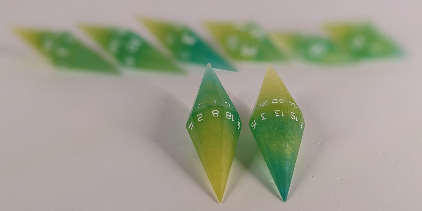 A stylized macro shot focusing heavily on 2 d20s from a yellow and teal swirl with white numbers handmade dice set in the foreground. The sharp diamond edges of these front resin dice are crisp, while the rest of the matching artisan dice collection forms a softly blurred background, creating depth.