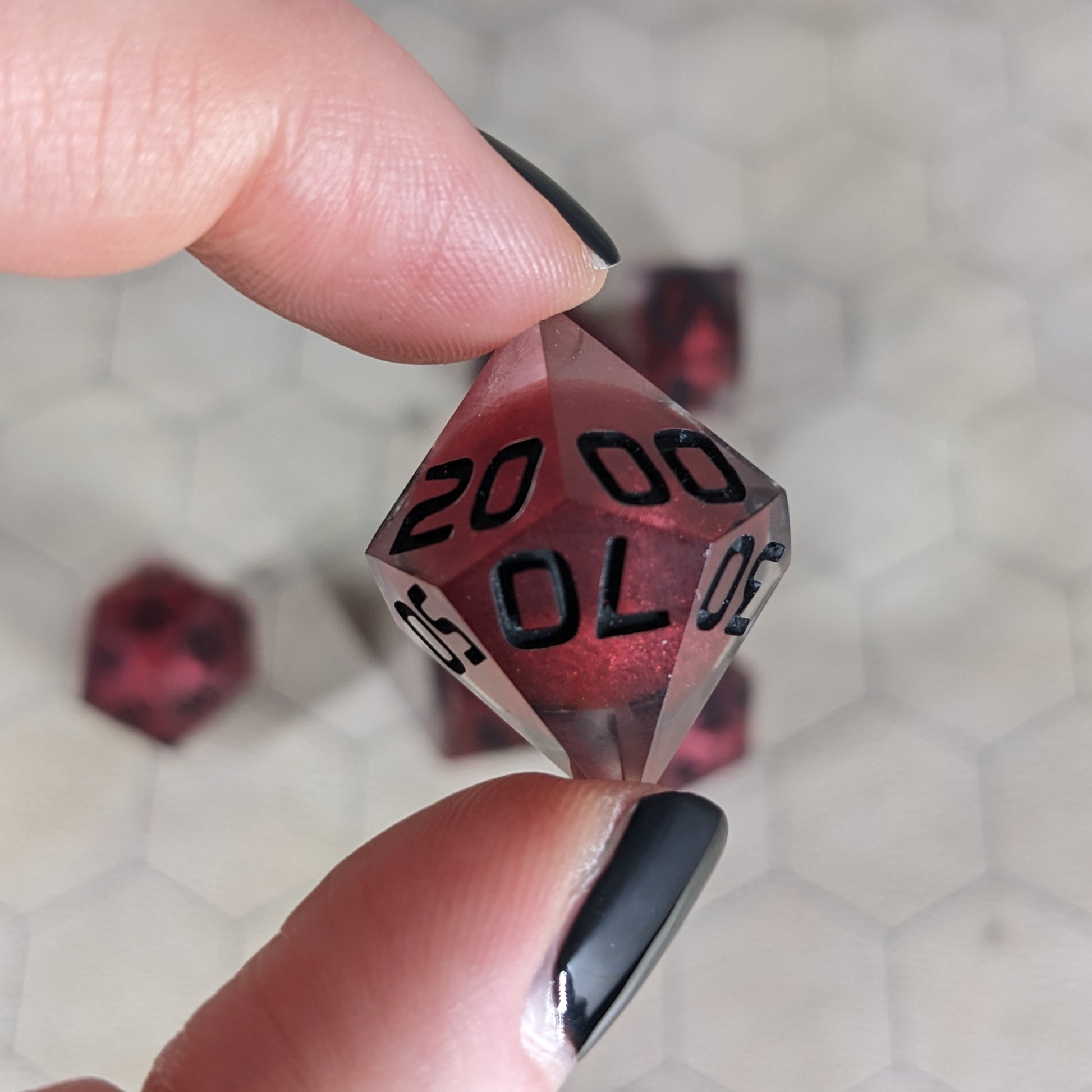 The d% die is being held up to the camera to show off the red, spherical insert and the dark glow the black numbers give in the clear shell. The 20, 00, and 70 faces are angled toward the camera.