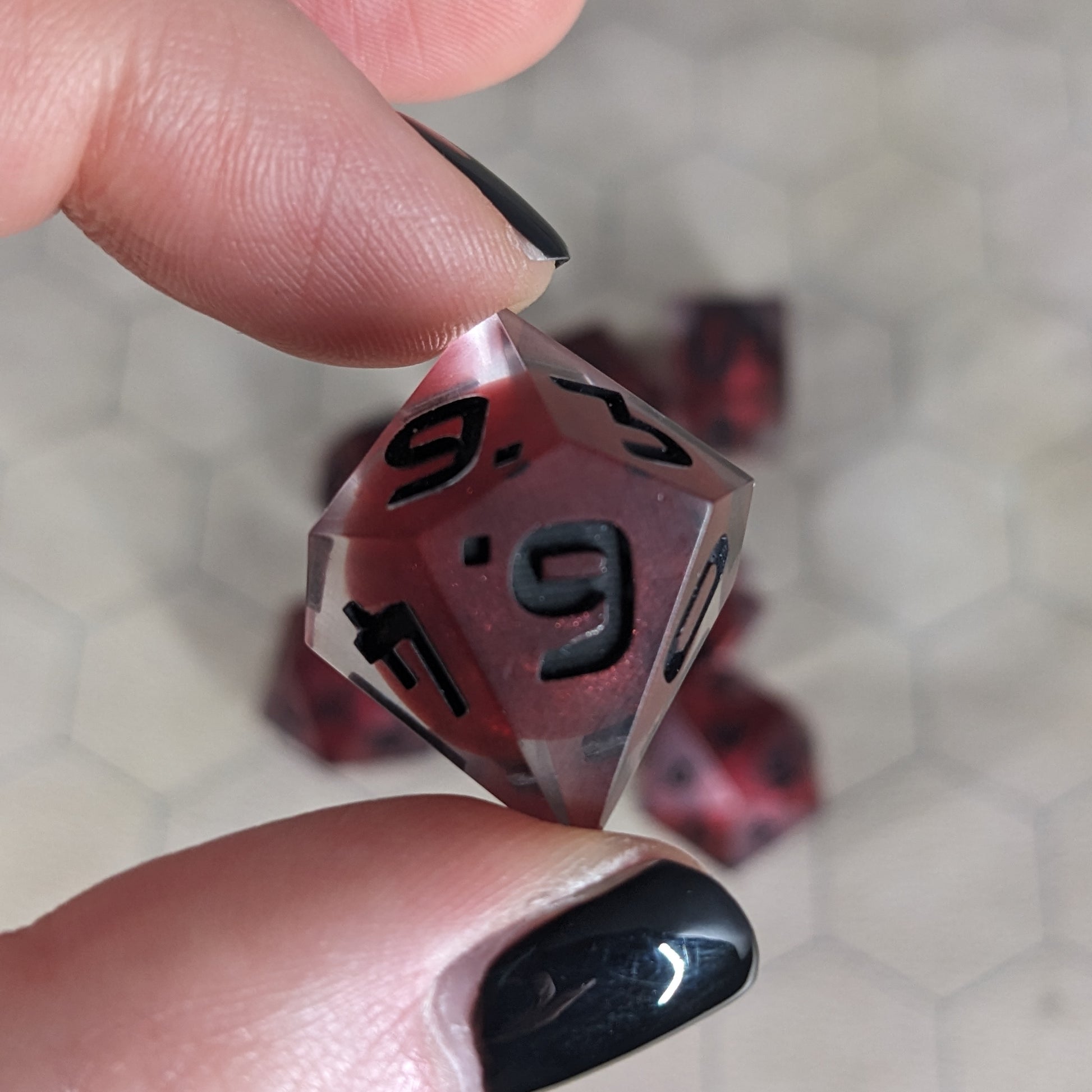 The d10 die is being held up to the camera to show off the red, spherical insert and the dark glow the black numbers give in the clear shell. The 6 face is most angled toward the camera.