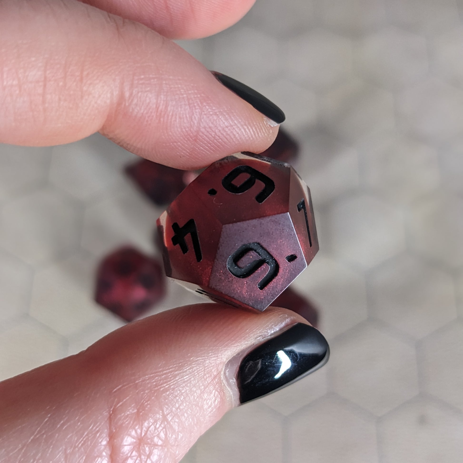 The d12 die is being held up to the camera to show off the red, spherical insert and the dark glow the black numbers give in the clear shell. The 6, 9, and 4 faces are angled toward the camera.