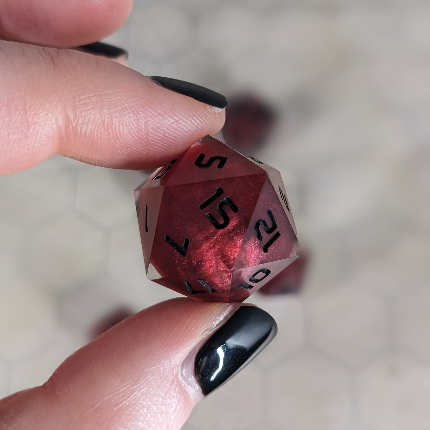 The d20 die is being held up to the camera to show off the red, spherical insert and the dark glow the black numbers give in the clear shell. The 15 face is most angled toward the camera.